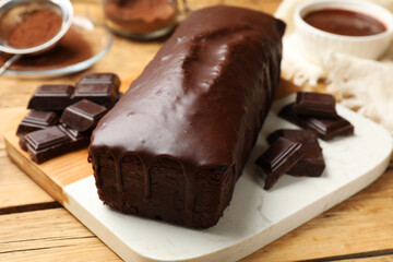 Tasty sponge cake and pieces of chocolate on wooden table, closeup