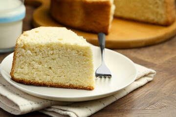 Piece of delicious sponge cake and fork on wooden table, closeup