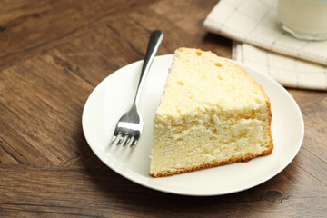 Piece of delicious sponge cake and fork on wooden table, closeup