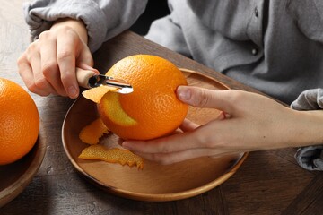 Woman zesting orange at wooden table, closeup