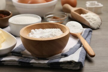 Baking powder in bowl and other products on wooden table, closeup