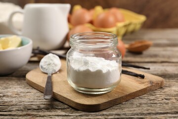 Baking powder in jar and spoon on wooden table, closeup