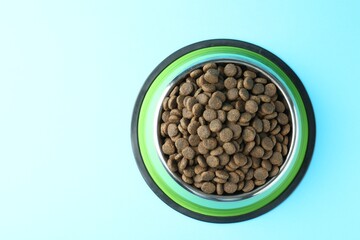 Dry pet food in feeding bowl on light blue background, top view. Space for text