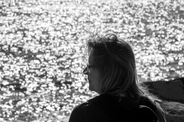 Frau mit schulterangem Haar schaut auf das Meer welches im Hintergrund in der Sonne glitzert