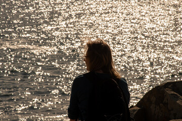 Frau mit schulterangem Haar schaut auf das Meer welches im Hintergrund in der Sonne glitzert