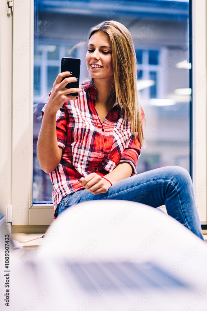 Poster charming young woman sitting on window sill with smartphone for taking selfie on frontal camera, fem