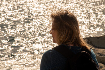 Frau mit schulterangem Haar schaut auf das Meer welches im Hintergrund in der Sonne glitzert