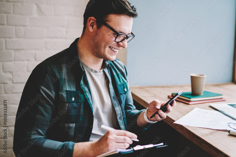 Poster cheerful young man laughing on funny video browsed on smartphone while working remotely in cafe ,smi