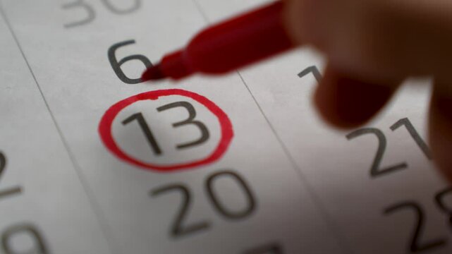 Female hand with pen mark on calendar date, close-up. Woman hand marking with a red pen on calendar circles the day, deadline concept
