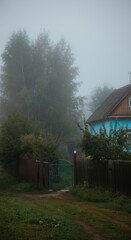 Misty morning landscape with blue cottage and lush greenery in tranquil countryside