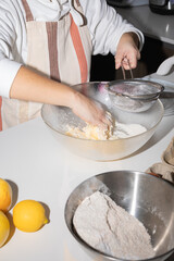 Close up hands of woman baking in kitchen sifting flour into mixing bowl with butter