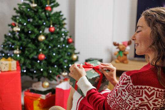 Young woman happy and smiling, happily celebrates all the gifts she has under the Christmas tree. Consumerism, shopping period.