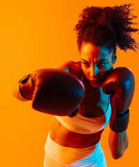 Sportive black hispanic woman wearing sportswear training boxing in fitness studio, colorful...
