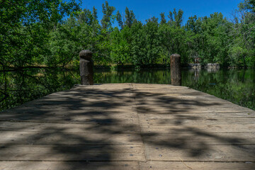 A rustic wooden pier surrounded by lush greenery and calm waters in the Bosque Finlandés of Rascafría, Spain. Ideal for nature, travel, and outdoor themes.