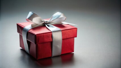 Obraz premium A red gift box tied with a silver ribbon sits on a grey surface, a symbol of celebration and thoughtfulness.