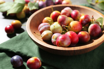 Ripe plums in bowl on grey table, closeup