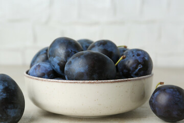 Ripe plums in bowl on light table, closeup