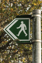  Small green and white walking man and arrow graphic sign on a sign post indicating a traffic free public path or track suitable for walking and exercise
