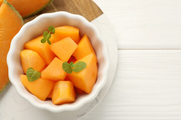 Pieces of Cantaloupe melon and mint in bowl on white wooden table, top view. Space for text