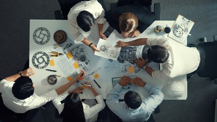 Top down aerial view of smart engineer team working together to design turbine engine. Professional technician discussing about jet engine construction while pointing at part of engine. Alimentation.