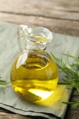 Cooking oil in jug and rosemary on wooden table, closeup