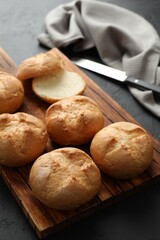 Board with homemade tasty buns on black textured table, closeup