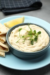 Delicious hummus in bowl, pita and lemon on table, closeup