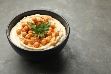 Delicious hummus with parsley, paprika and chickpeas in bowl on grey table, closeup. Space for text