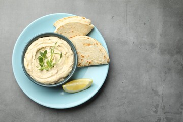 Delicious hummus in bowl, pita and lemon on grey table, top view. Space for text