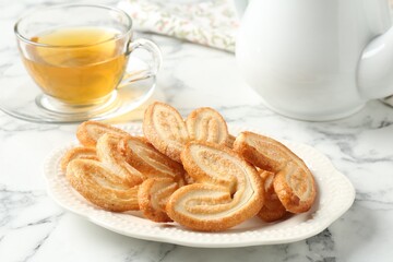 Delicious palmier cookies with tea on white marble table, closeup
