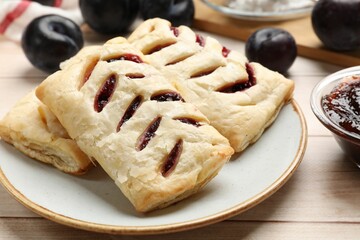 Delicious puff pastries and plums on white wooden table, closeup