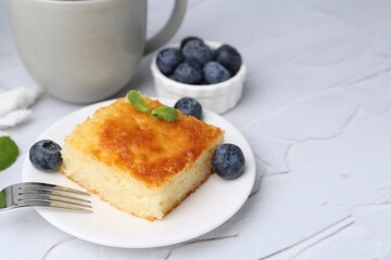 Slice of tasty semolina cake served on white textured table, closeup. Space for text