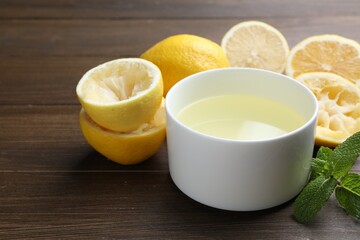 Fresh lemon juice in bowl, fruits and mint on wooden table, closeup