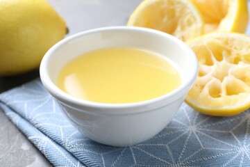 Fresh lemon juice in bowl and fruits on table, closeup
