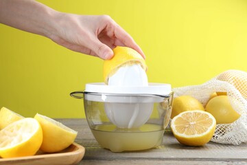 Woman with lemon using juicer at wooden table, closeup