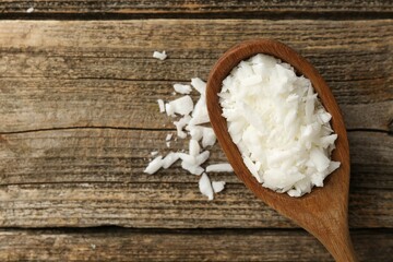 White soy wax flakes in spoon on wooden table, top view. Space for text