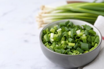 Chopped green onion in bowl on white table, closeup. Space for text