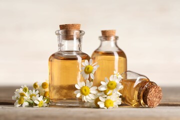 Bottles of essential oil and chamomile flowers on wooden table, closeup