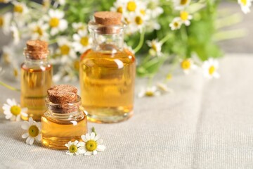 Bottles of essential oil and chamomile flowers on cloth, closeup. Space for text