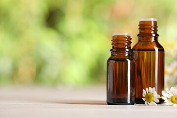Bottles of essential oil and chamomile flowers on white wooden table against blurred background, closeup. Space for text