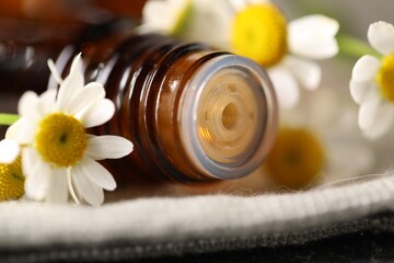 Bottle of essential oil and chamomile flowers on cloth