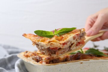 Woman taking piece of delicious cooked lasagna with basil at table, closeup