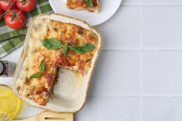 Delicious cooked lasagna with basil served on white tiled table, flat lay. Space for text