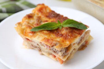 Piece of delicious cooked lasagna with basil on plate, closeup