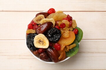 Mix of different dried fruits in bowl on white wooden table, top view