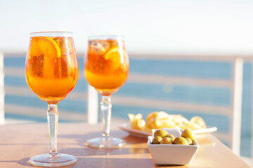 Aperol spritz cocktail glasses with olives and potatoes chips aperitif, very Mediterranean. Sea views, gastronomy and travel concept.