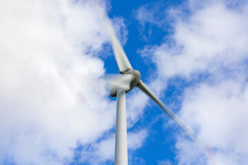 Windrad in Bewegung mit Bewegungsunsch&auml;rfe vor blauem Himmel mit Wolken