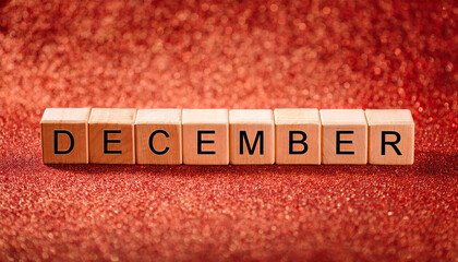 Wooden cubes with text DECEMBER on red glittering backdrop. Winter season. New Year, Christmas