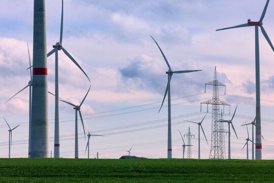 Feld mit Windr&auml;dern und Strommasten bei Sonnenuntergang