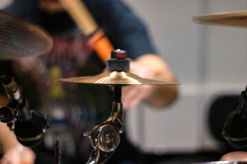 Close up of cymbals with drummer playing drums in a blurry background.